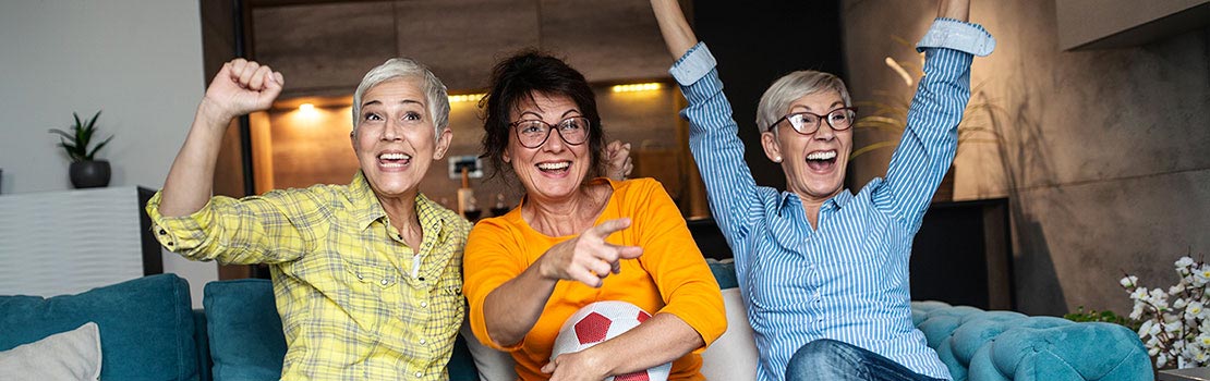 Three senior women watching a soccer game and cheering.